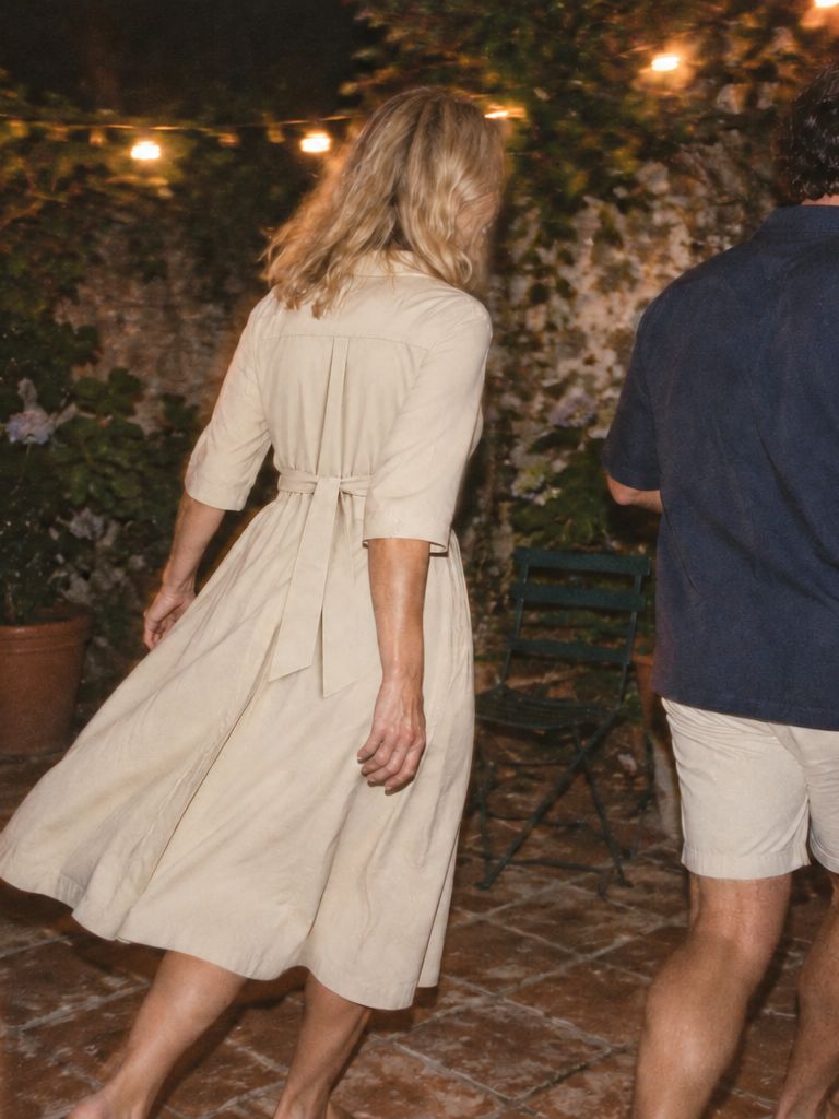 Friends dance on a patio under string lights at night, a woman in the bone shirt dress and a man in the ink camp-collar shirt